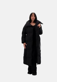 Abrigo acolchado negro con cuello sobredimensionado, largo, botones en el frente y bolsillos laterales. Textura suave y diseño minimalista.