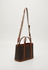 Brašna s uzorkom u smeškastoj boji s kožnim detaljima, dvostrukim ručkama na vrhu i odvojivim remenom s natpisom "MICHAEL KORS".