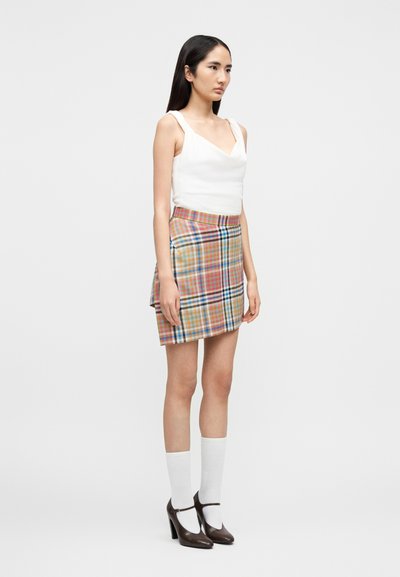 Γυναίκα με λευκό αμάνικο τοπ, πολύχρωμη καρό μίνι φούστα, λευκές κάλτσες μέχρι τον αστράγαλο και καφέ ψηλοτάκουνα παπούτσια Mary Jane.