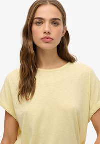 Camiseta de algodón amarilla con cuello redondo, corte relajado, mangas cortas enrolladas y un acabado suave y texturizado. Sin patrones ni acentos visibles.