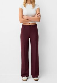 Burgundy vida byxor med en mjuk tyg, som har framknäppning och framfickor, ihop med en åtsittande vit topp och sneakers.