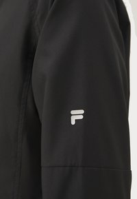 Mustra mustang mustriga musta jope, mille varrukal on ülemisel õlal väike valge stiliseeritud "F" logo.