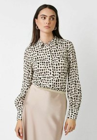 Long-sleeve button-up shirt in cream with a black geometric pattern, featuring a classic collar and cuffs. Textured, lightweight fabric.