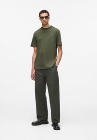 Tricou din bumbac de culoare verde măsliniu și pantaloni largi asortati. Pantofi negri. Accesoriu constă în ochelari de soare dreptunghiulari cu ramă subțire.