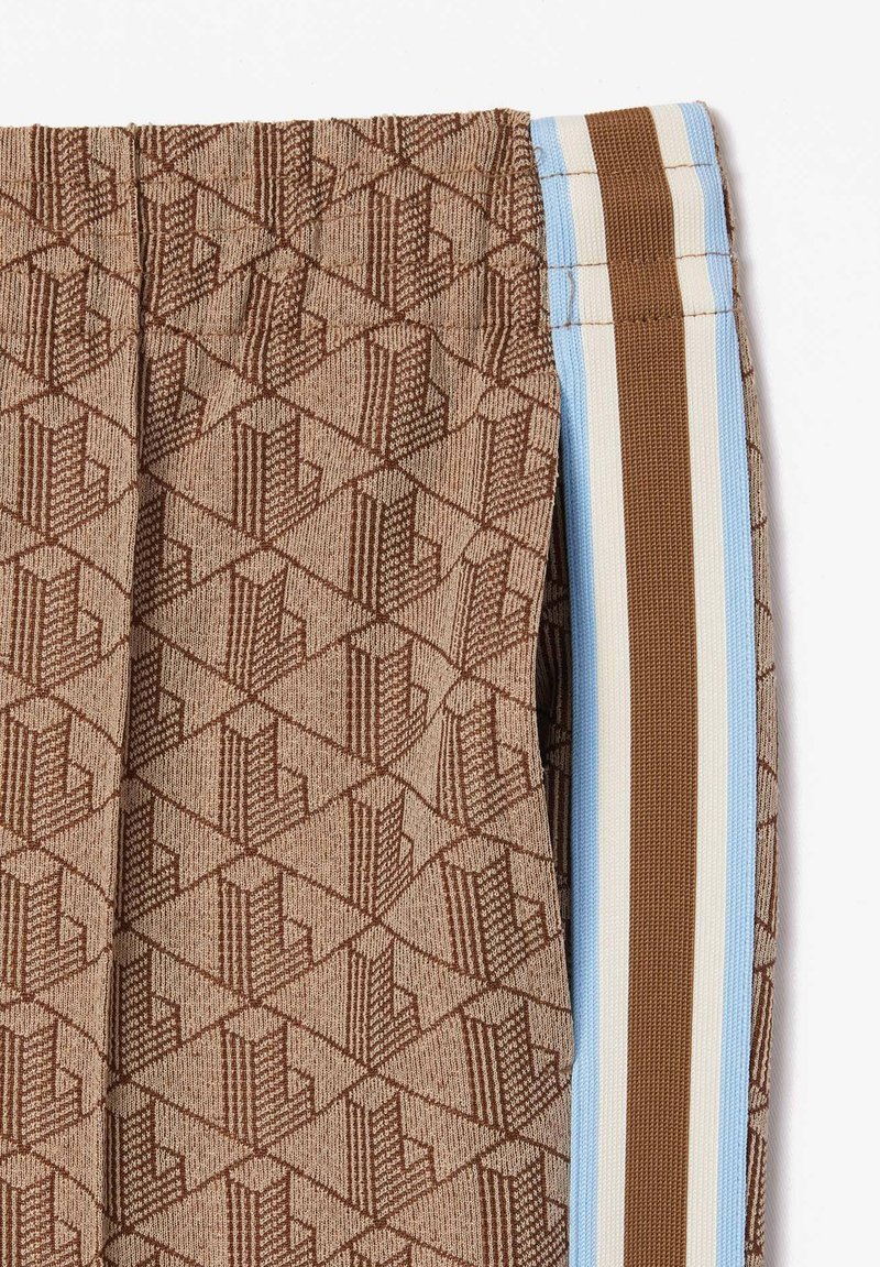 Brązowe spodnie w wzory z geometryczną teksturą, z bocznymi paskami w jasnym niebieskim i brązowym kolorze. Tkanina jest gładka, a fason dopasowany.