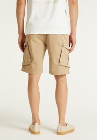 Shorts cargo beiges avec deux grandes poches latérales, dotés d'une taille plate et d'un ourlet se terminant juste au-dessus du genou. Associés à des chaussures de couleur crème.