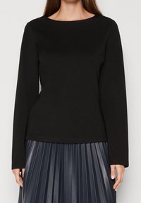 Haut noir à manches longues en coton, avec un col rond et une coupe ajustée. Associé à une jupe plissée bleu marine pour le contraste.