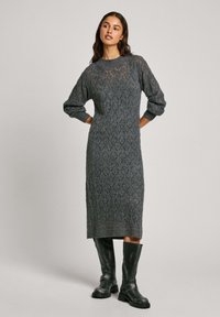 Abito grigio lavorato a maglia con texture a motivo diamante, maniche larghe e scollatura tonda. Abbinato a stivali neri in pelle alta fino al ginocchio.