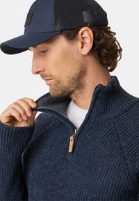 Marineblå ribstrikket sweater med høj krave og lynlås, parret med en marineblå kasket med et struktureret bagpanel og et logo-patch.