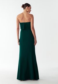 Zielona, sukienka wieczorowa bez ramiączek o dopasowanym kształcie, gładkiej fakturze i rozkloszowanym dole, z delikatną plisą z tyłu i zamkiem błyskawicznym.