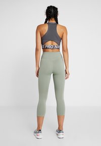 Sportovní podprsenka v tmavě šedé barvě s vykrojeným zadním dílem a značkovým pásem. Legíny s vysokým pasem v jemně zelené barvě s hladkým povrchem.