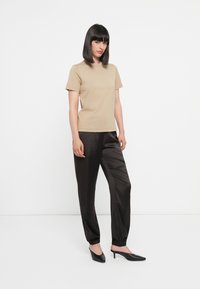 Beige cotton t-shirt paired with black satin joggers featuring elasticated cuffs and pointy black heels. Simple, fitted design.
