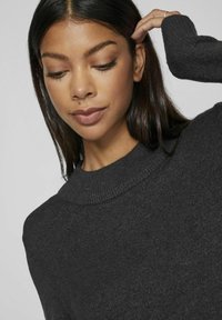 Maglione a maglia grigio scuro con scollatura rotonda a coste e tessuto testurizzato, con una mano che solleva parzialmente i capelli.