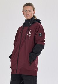 Bordeaux en zwarte ritsjack met hoge kraag, verstelbare trekkoorden en logo-accenten. Heeft zijzakken en lange mouwen.