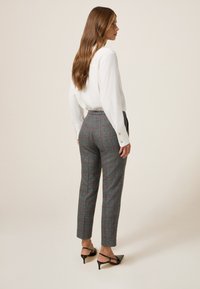 Pantaloni a quadri grigi con accenti rossi, vita alta, vestibilità affusolata e tessuto texturizzato; abbinati a una camicia bianca con colletto.