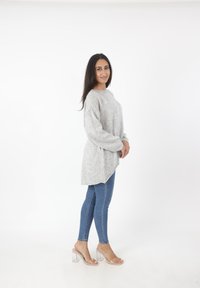Lichtgrijze oversized gebreide trui met lange mouwen, een hoge-lage zoom, gecombineerd met blauwe skinny jeans en doorschijnende block-heeled sandalen.