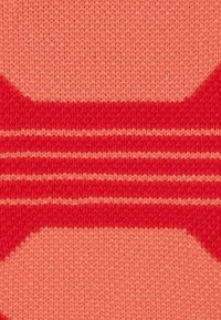 Tessuto lavorato a maglia in tonalità corallo e rosso, caratterizzato da un motivo geometrico con strisce e una texture liscia, creando un contrasto tra le sezioni.