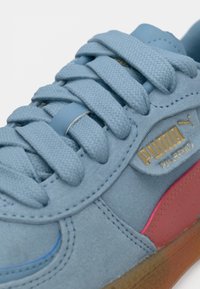 Svetlo modri antilopasti športni copati z teksturiranimi vezalkami, gumo podplatom in rožnatimi poudarki. Zlata Puma oznaka na strani. Ima zaobljen toe in šivano podrobnost.