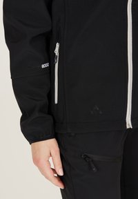 Black waterproof jacket with white zippers, featuring a high collar, adjustable cuffs, and textured fabric. Includes logo detail on sleeve.