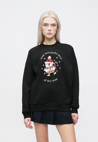 Melna sudraba jaka ar izšūtu pingvīnu, kuram virsū ir Ziemassvētku cepure un svītrainā krekls, ap to ir teksts "Brīnišķīgākais gada laiks".