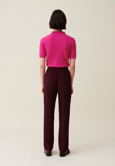 Polo aderente rosa a maniche corte con colletto abbinato a pantaloni tailored bordeaux scuro. Il materiale sembra morbido con una texture liscia.