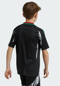 Svart sportströja med gröna och röda krageaccenter, texturerad tyg och kontrasterande vita tribalmönster på sidorna. Korta ärmar.