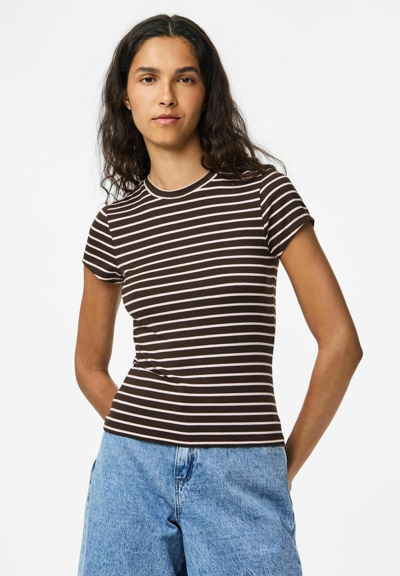 Ruda ir balta dryžuota trumpomis rankovėmis marškinėliai su prigludusia forma ir apvaliu kaklu, pagaminti iš minkštos medžiagos. Suderinti su šviesiai mėlynais džinsiniais šortais.