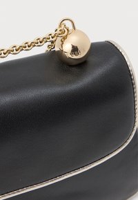 Melnā ādas somiņa ar sudraba apdari, zelta ķēdes siksniņu un apaļu zelta piekari, kurā ir iespiests "FURLA", pievienots ķēdei.