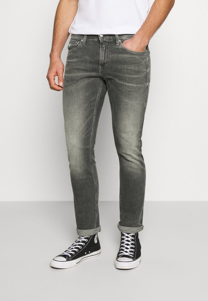 Mörkgrå jeans i smal passform med subtila blekningseffekter, fem fickor och uppvikta fållar, kombinerade med svarta höga sneakers.