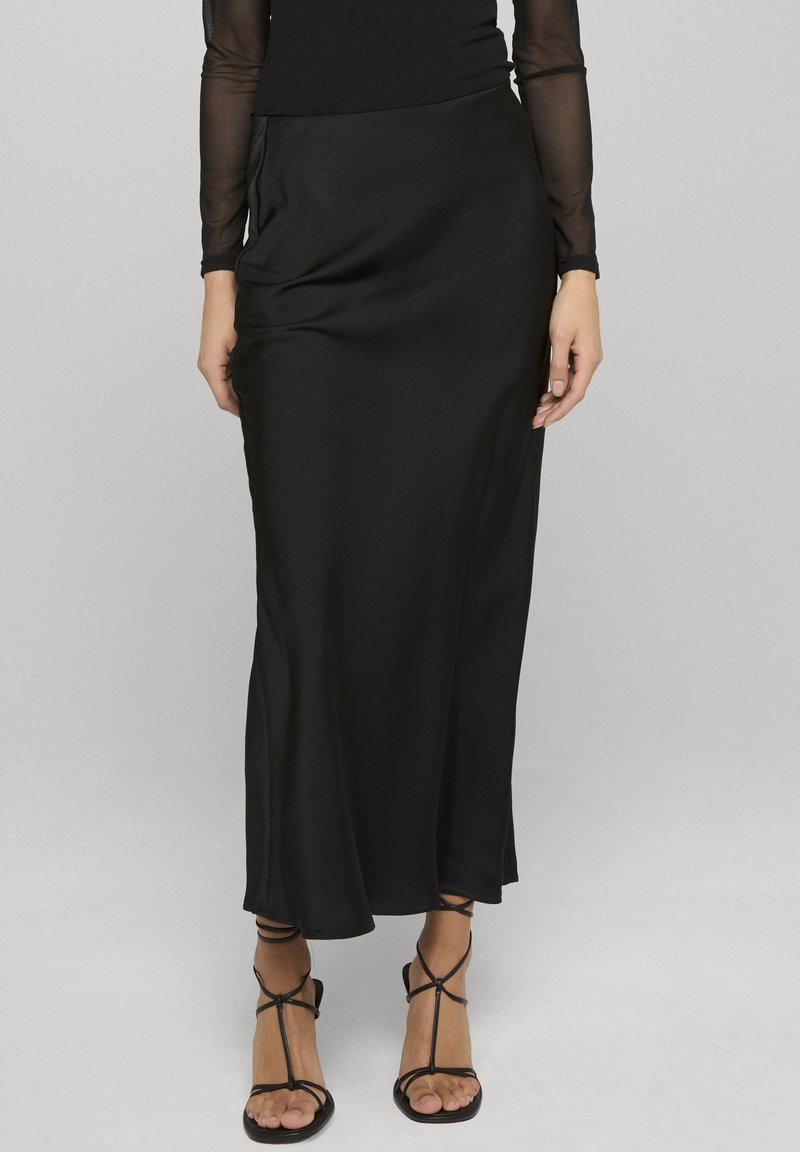 Mustast satiinist maksiseelik, millel on siledapinnaline tekstuur, kõrge vöökoht ja küljetaskud. Koos mustade rihmikute sandaalidega.