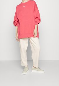 Nike överdimensionerad röd sweatshirtd med ballongsärmar, parat med krämfärgade smalbyxor och ljusgrå sneakers. Vit logotyp på bröstet.