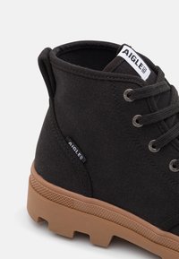 Stivale alla caviglia in tessuto nero con occhielli silver, lacci e suola in gomma marrone. Presenta un'etichetta con "AIGLE" sulla parte superiore.