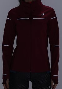 Burgundowa kurtka sportowa z wysokim kołnierzem, zamek błyskawiczny na całej długości oraz odblaskowe białe akcenty na rękawach i klatce piersiowej. Elastyczny materiał, dopasowany krój.