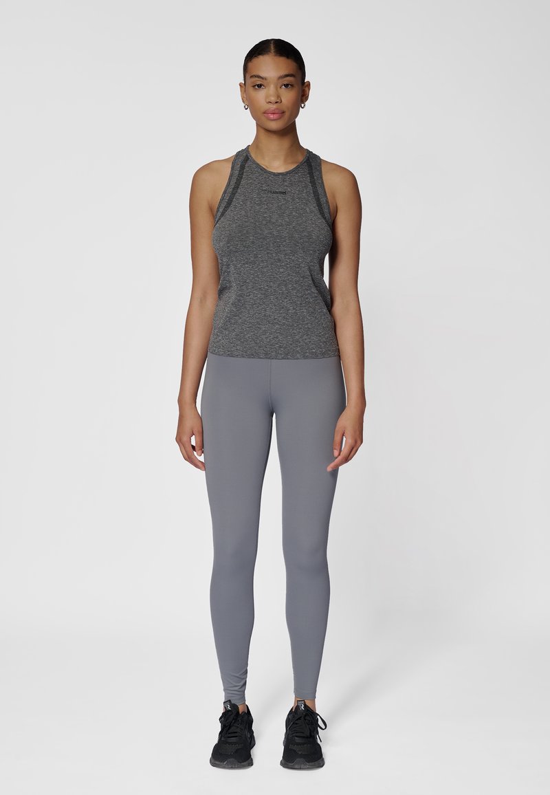 Szary sportowy top na ramiączkach typu racerback, zestawiony z jasnoszarymi legginsami. Charakteryzuje się gładką teksturą i czarnymi tenisówkami.