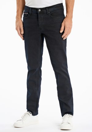 Dark blue denim jeans with a slim fit, five-pocket design, and a silver button closure, paired with white sneakers on a plain background.