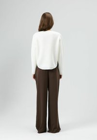 Witte gebreide trui met een ronde halslijn, gecombineerd met hoogwater, loszittende bruine broek. De textuur ziet er zacht en comfortabel uit.