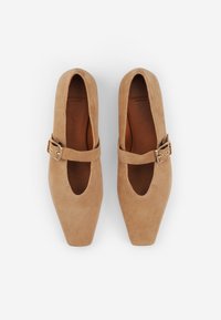 Beige semišové boty se čtveratým špičkou, které mají výřezový detail a přezku kolem kotníku pro bezpečné uchycení.
