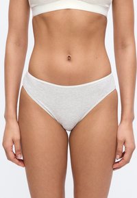 Γυναίκα που φορά γκρι ανοιχτό βαμβακερό εσώρουχο και ταιριαστό λευκό σουτιέν, στέκεται μπροστά σε μια απλή λευκή επιφάνεια.