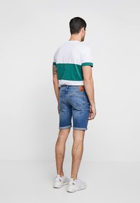 Lyhythihainen miesten paita valkoisena ja vihreänä, yhdistettynä sinisiin farkkushortseihin. Shortseissa on kääritty helma ja niissä on takataskut.