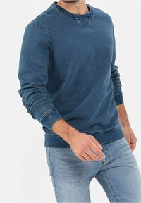 Felpa di cotone blu con scollo a girocollo, polsini a coste e finitura testurizzata, indossata con jeans in denim chiaro.