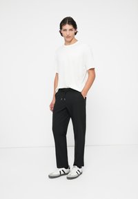 Pantaloni de trening negri cu talie cu șnur și buzunare laterale, asortați cu un tricou alb cu guler rotund și adidași albi cu accente negre.