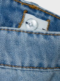 Svetlo modra denim tkanina z vidnimi šivi, ki ima plastičen gumb in belo tkanino z oznako, pritrjeno znotraj pasu.