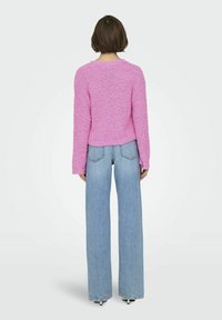 Maglione rosa testurizzato con maniche lunghe, scollo rotondo e taglio cropped. Abbinato a jeans a gamba larga di un blu chiaro, che mostra uno stile casual.