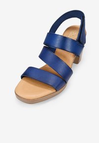 Sandal de cuero azul con tres correas horizontales, punta abierta y un tacón bajo. Plantilla de color marrón claro, superficie lisa y diseño limpio.
