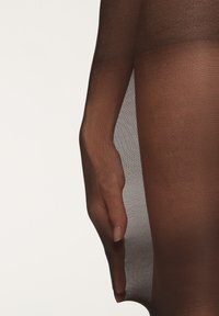 Genomskinliga svarta leggings med en mjuk textur, som visar en hand som försiktigt håller tyget mot en ljus bakgrund.