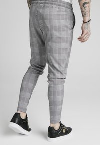 Szare spodnie dresowe w kratę z elastycznym pasem, zwężanymi nogawkami i bocznymi kieszeniami. Połączone z czarnymi sneakersami z złotymi akcentami.