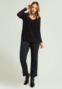 Schwarzes langärmliges Oberteil mit V-Ausschnitt, kombiniert mit schwarzen ausgestellten Jeans und Stiefeletten, betont glatten Stoff und lockeren Sitz.