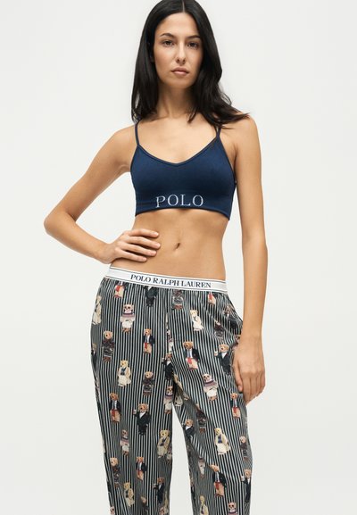 Femme portant un crop top bleu marine avec le texte "POLO" et un pantalon rayé avec différentes illustrations d'ours en peluche.