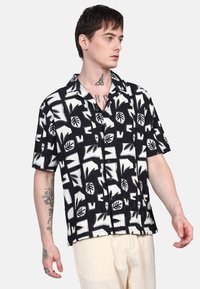 La camicia a maniche corte presenta un motivo a foglie in bianco e nero, un tessuto testurizzato e una vestibilità comoda con colletto a bottoni.