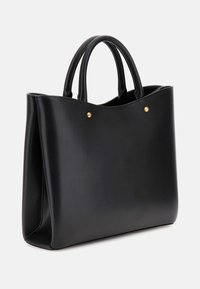 Sac en toile en cuir noir avec une texture lisse, des bords arrondis, deux poignées et des clous dorés à l'avant. Design spacieux et structuré.